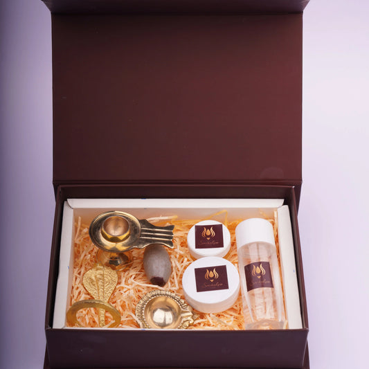 Gift box with brass spiritual items, containers, clear bottle and a stone on straw filling