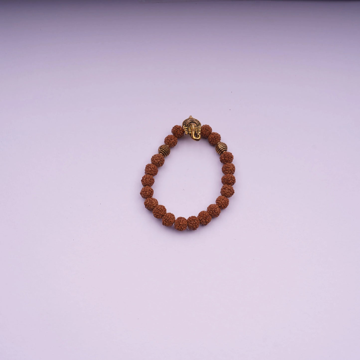 Rudraksha bead bracelet with gold-tone Ganesh charm on light purple background