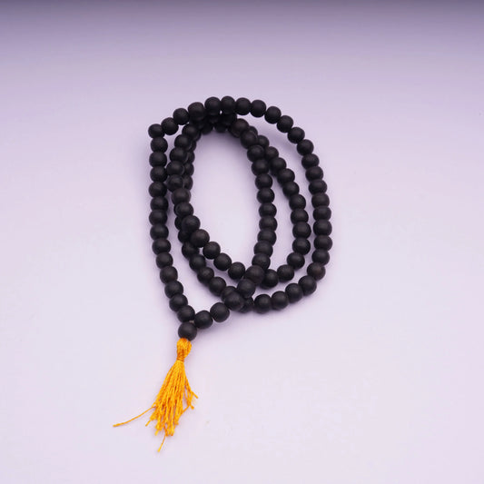 Black gemstone mala beads with yellow tassel on a light background