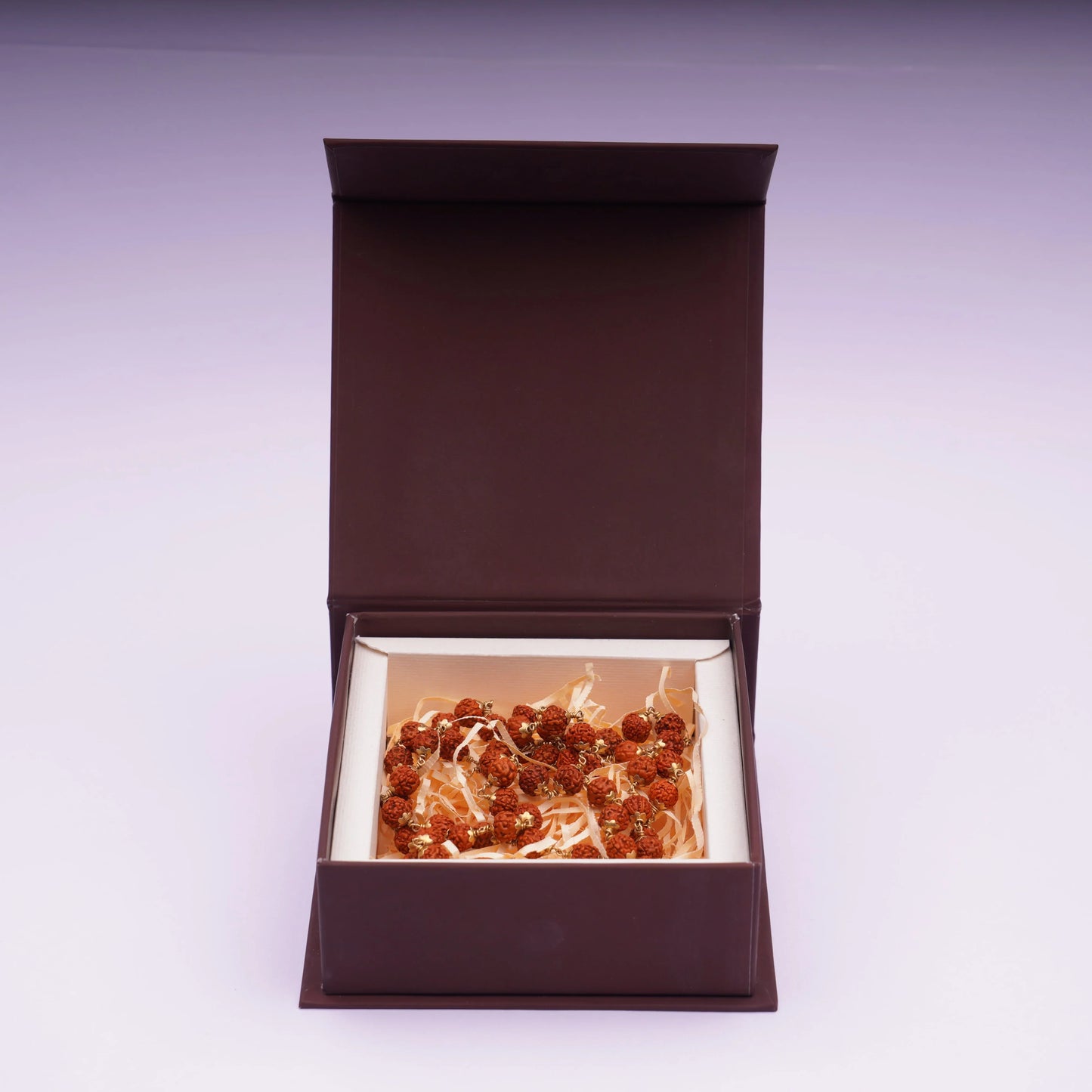 Rudraksha mala with brass plated beads displayed in a brown gift box on light background