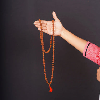 Hand holding a rudraksha mala bead necklace with orange tassel on black background