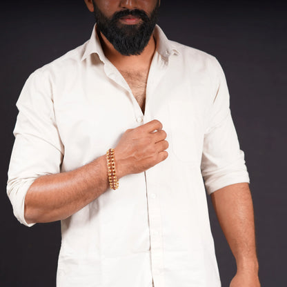 Man wearing a beige shirt and beaded stone bracelet on wrist against dark background
