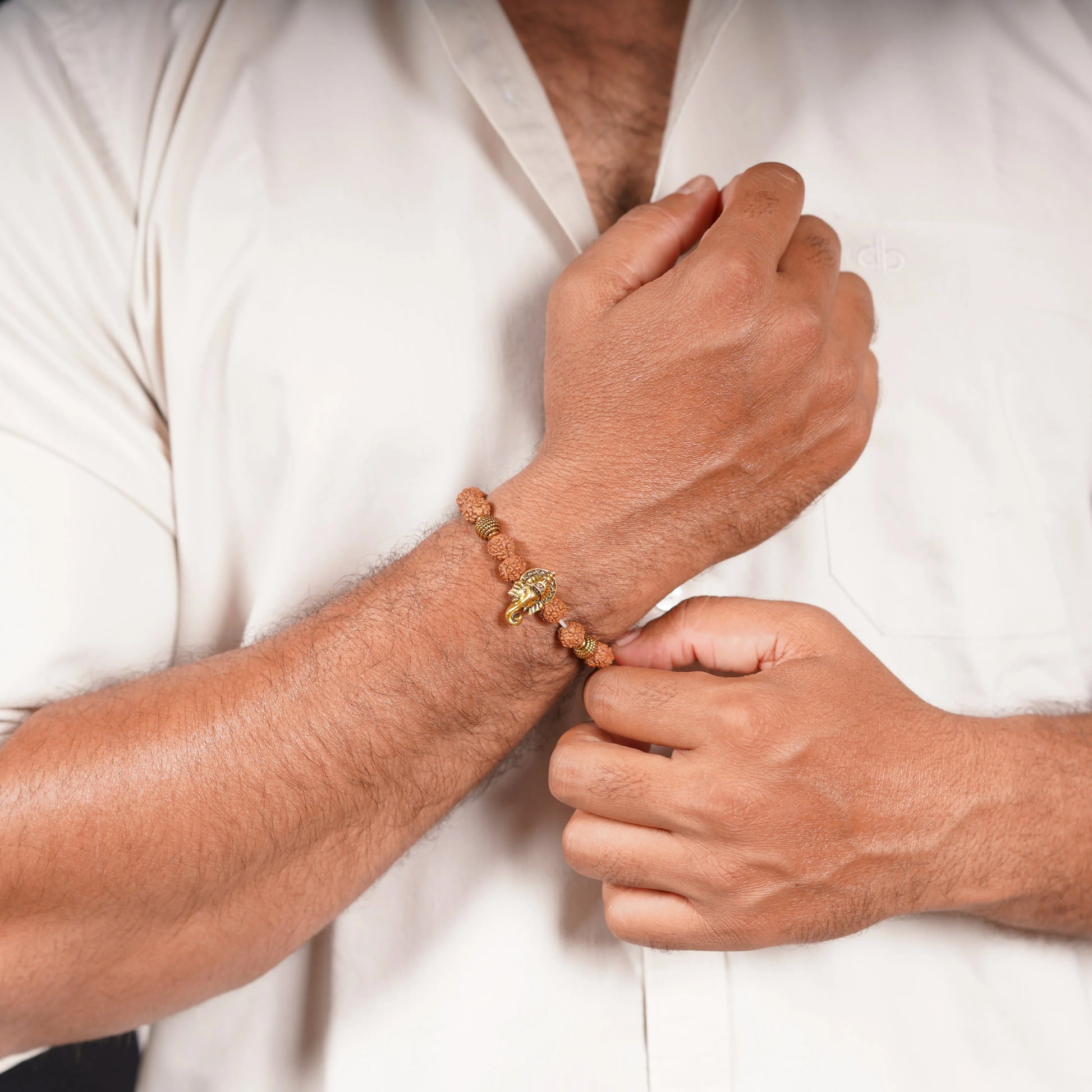 Man wearing a rudraksha bead bracelet with a gold elephant charm on wrist