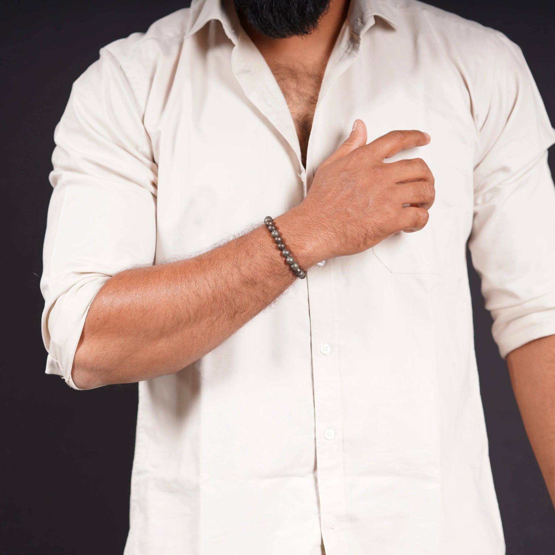 Man wearing a beaded stone bracelet with a beige shirt on a black background