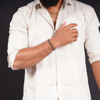 Man wearing a beaded stone bracelet with a beige shirt on a black background