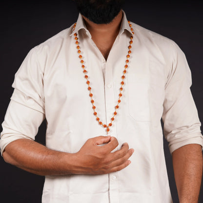 Man wearing a long orange gemstone mala necklace over a white shirt, dark background