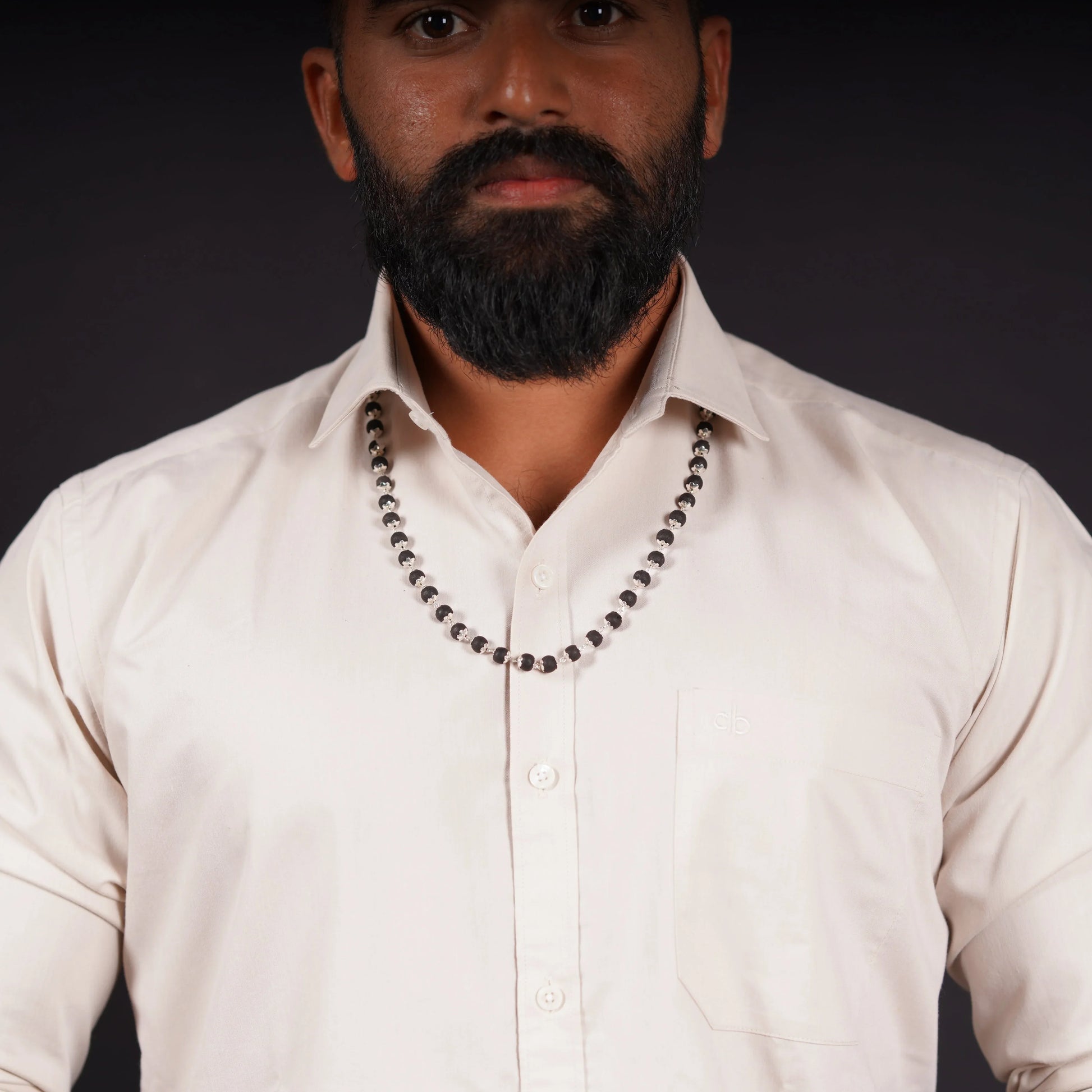 Man wearing beaded stone necklace over cream dress shirt on dark background