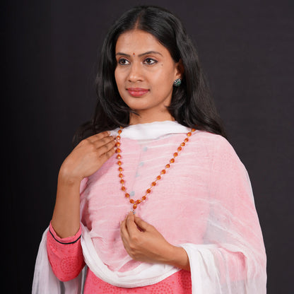 Woman wearing traditional attire and an orange gemstone bead necklace on black background