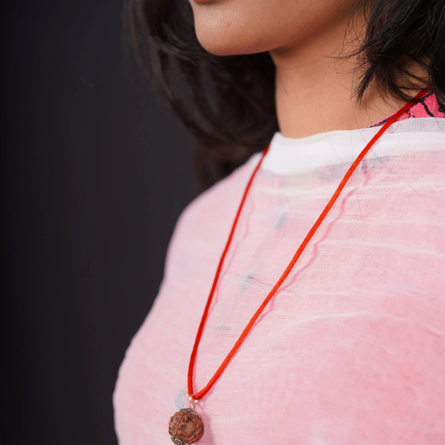 Woman wearing a Rudraksha pendant on red thread, close-up against a black background.