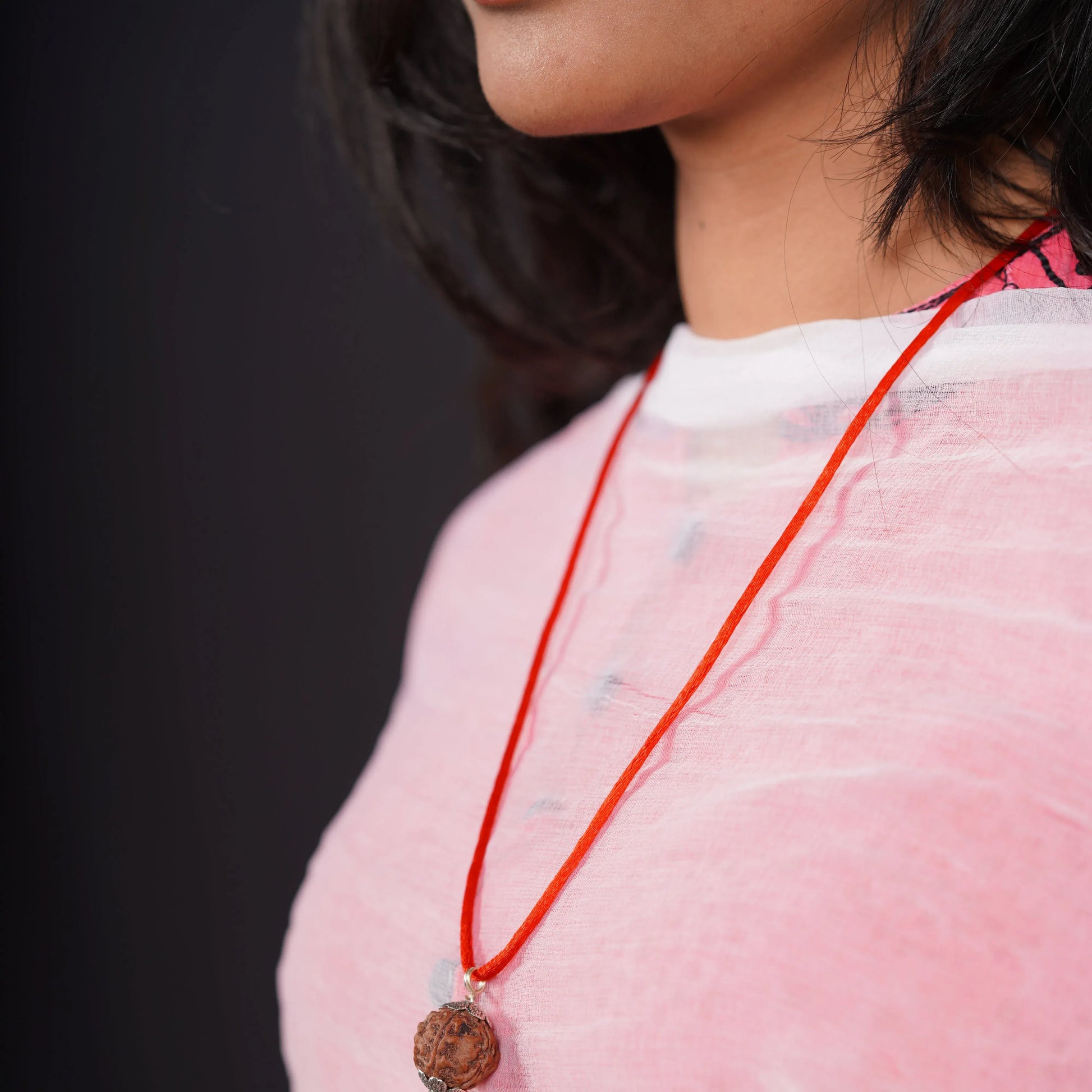 Woman wearing a 5 Mukhi Rudraksha pendant on red thread, close-up against a black background.