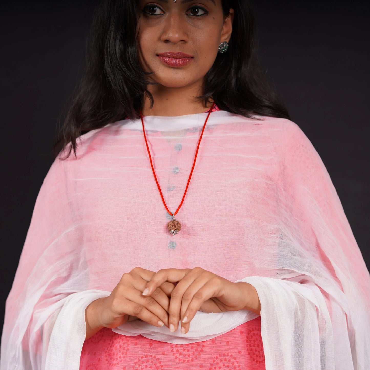 Woman wearing a rudraksha pendant necklace on a red cord, dressed in a light pink kurta.