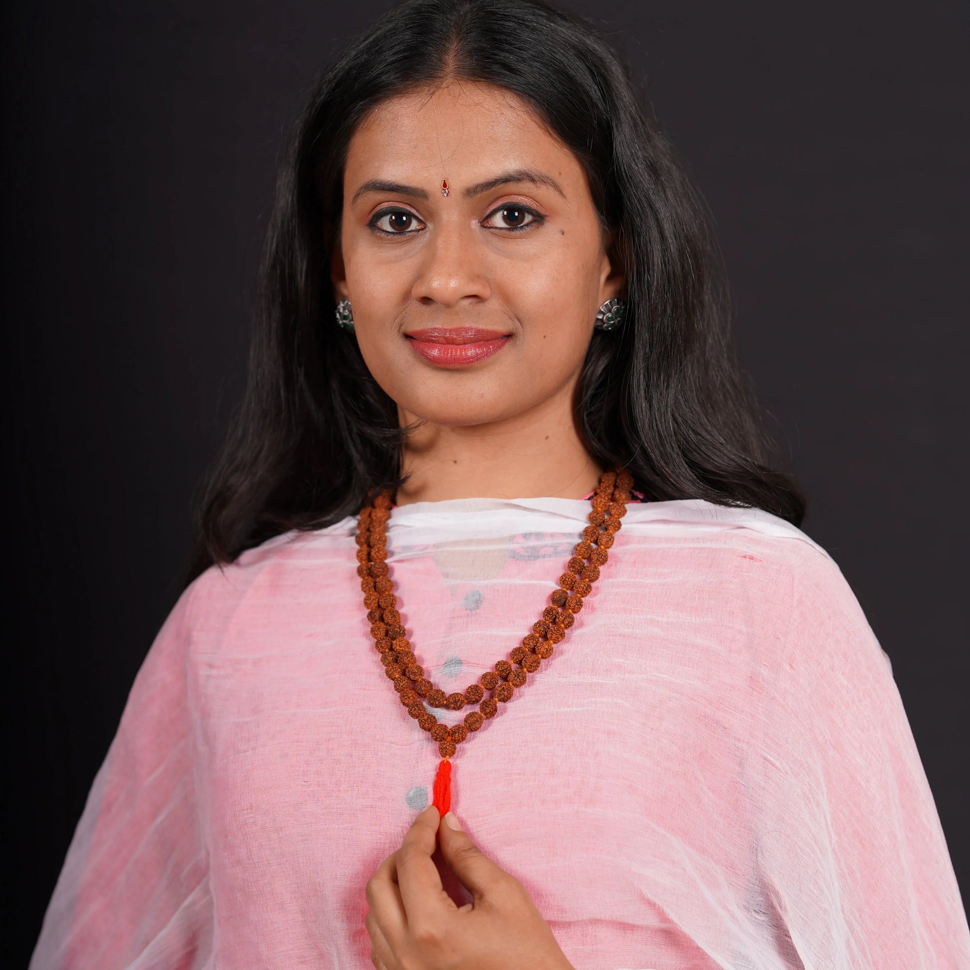 Woman wearing double rudraksha mala necklace with red tassel, traditional attire, black background