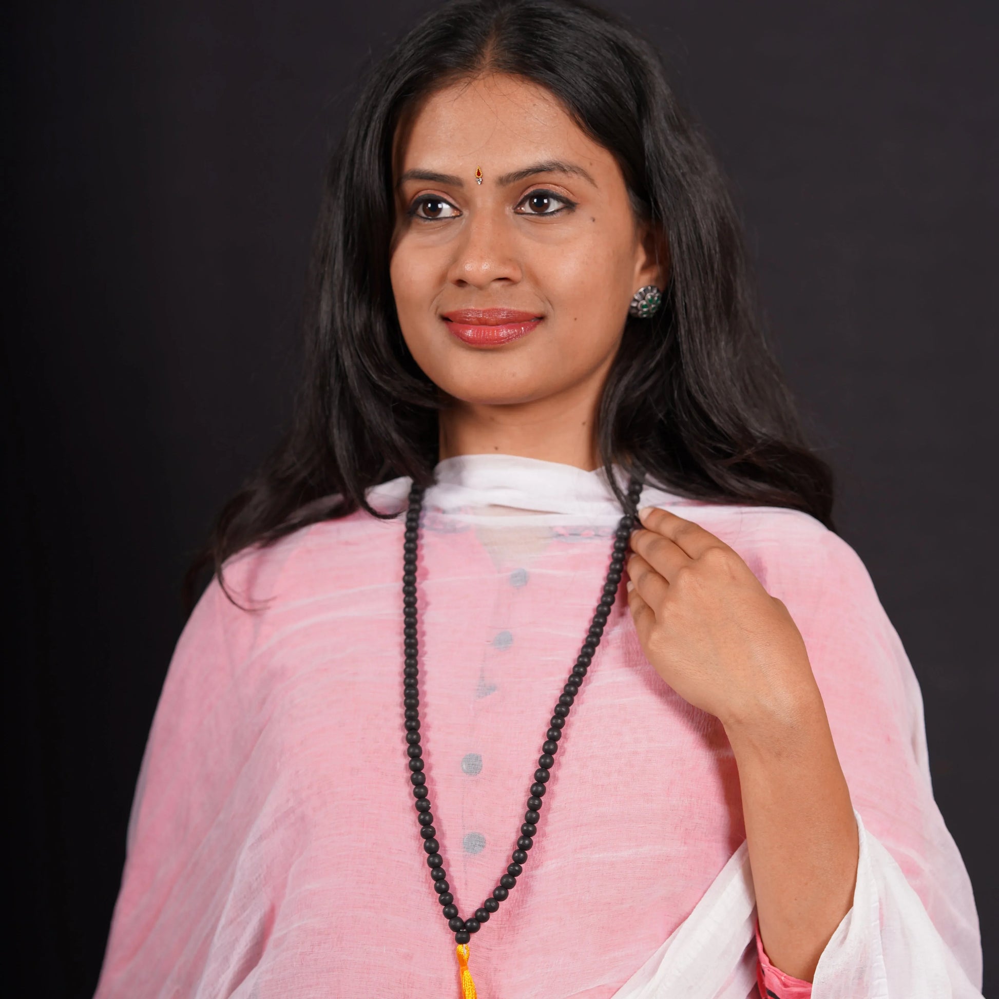 Woman in pink kurta wearing long black beaded mala necklace on black background
