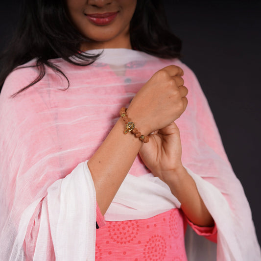 Woman wearing a rudraksha beaded bracelet with gold charm, pink and white traditional attire