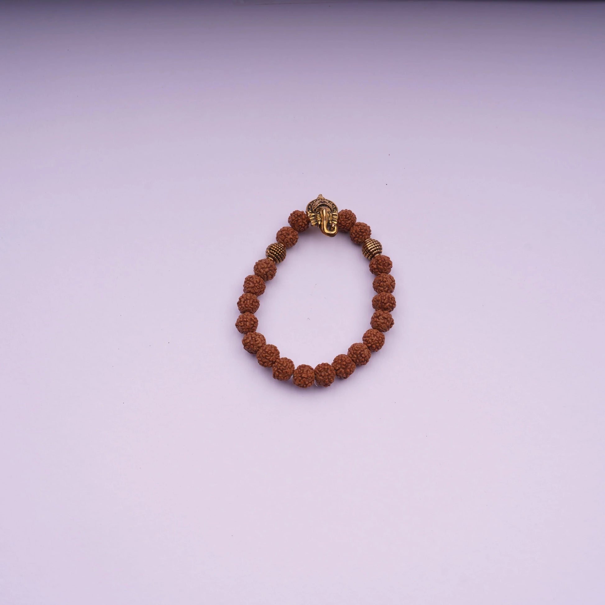 Rudraksha bead bracelet with gold-tone Ganesh charm on light purple background