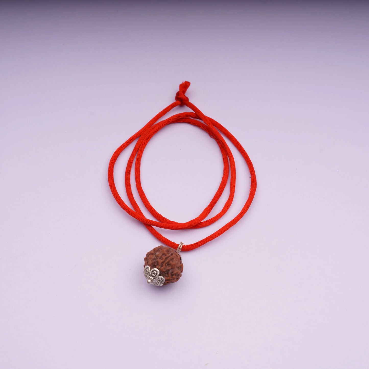 Rudraksha bead pendant on red thread necklace with silver caps on light background