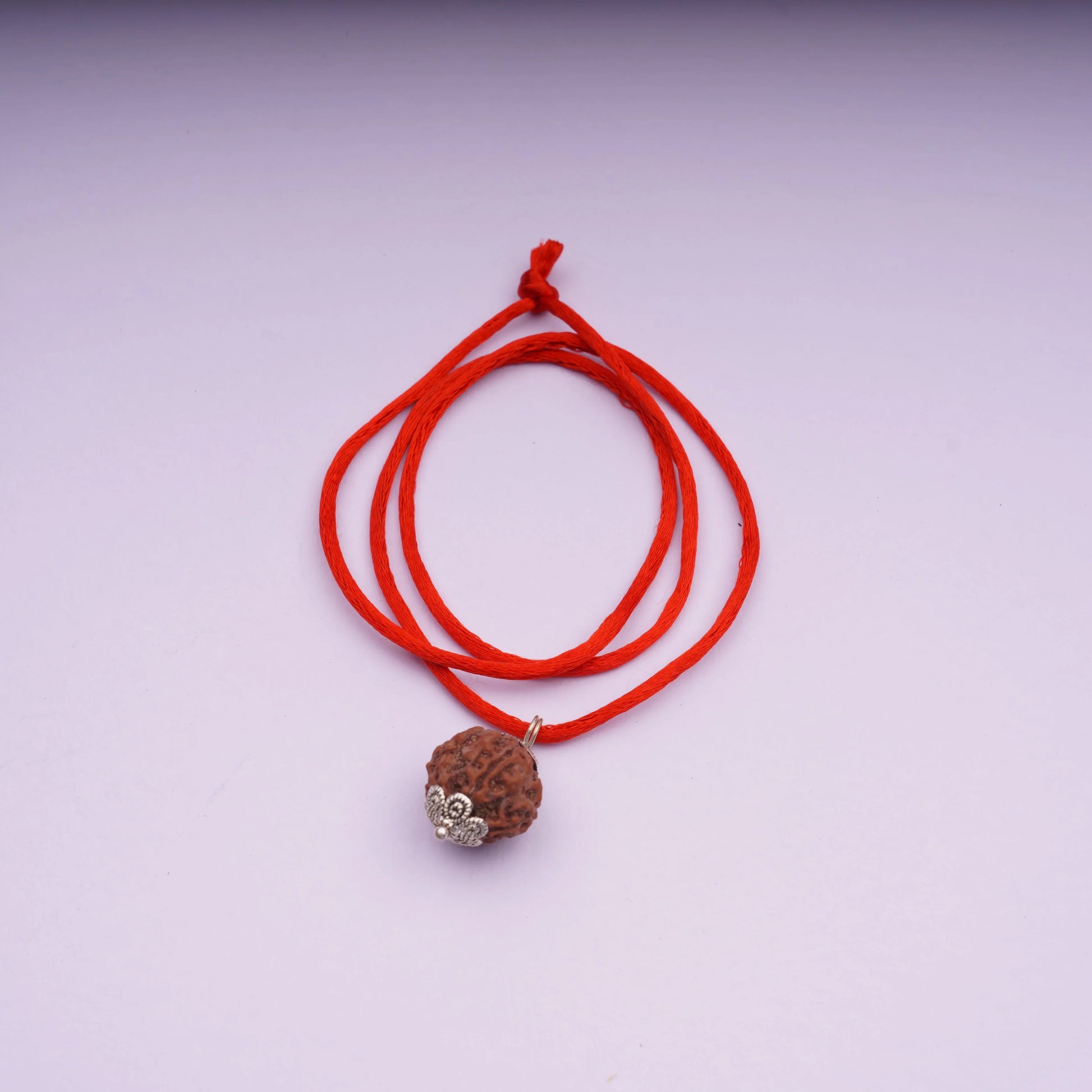 Rudraksha bead pendant on red thread necklace with silver caps on light background