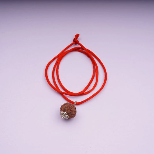 Rudraksha bead pendant on red thread necklace with silver caps on light background