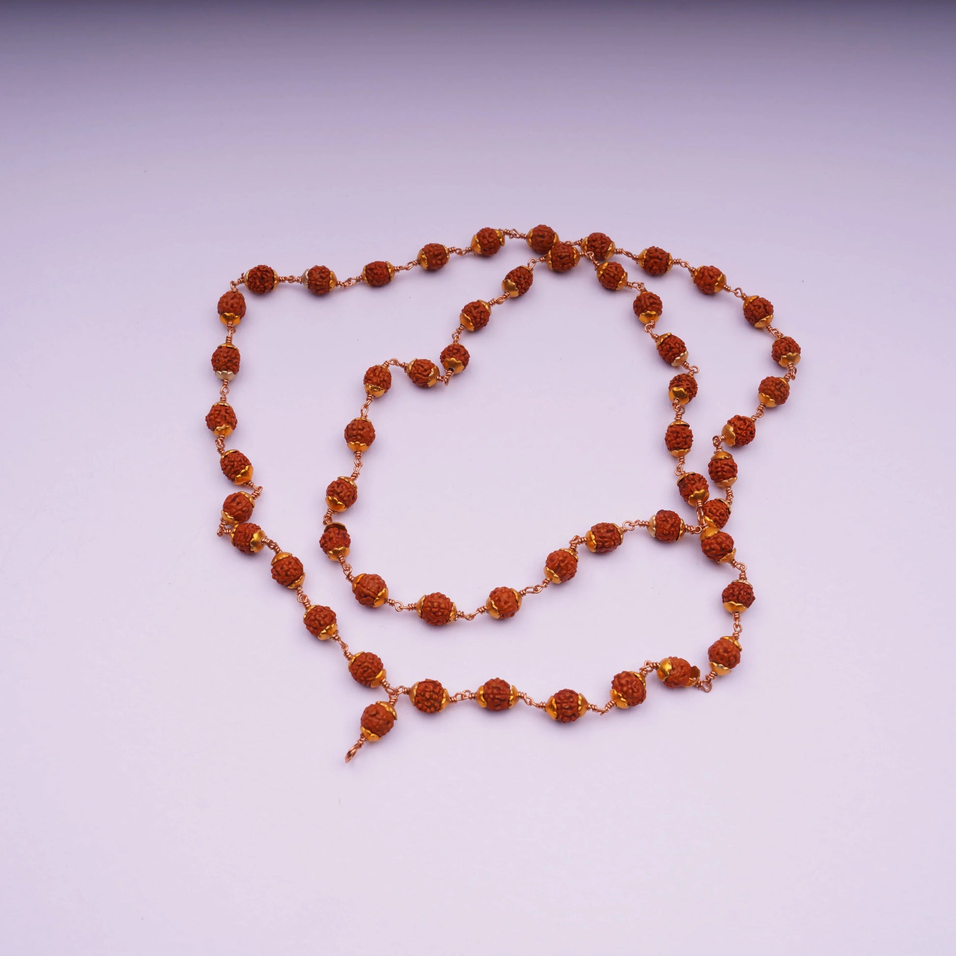 Rudraksha bead mala necklace with gold-tone links on a light pink background