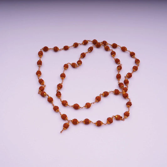 Rudraksha bead mala necklace with gold-tone links on a light pink background