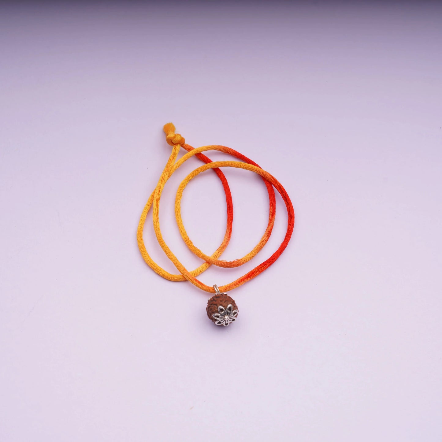Orange and yellow thread necklace with Rudraksha pendant on light background