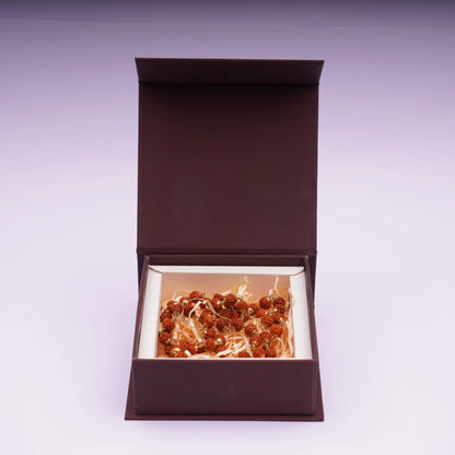 Rudraksha mala with brass plated beads displayed in a brown gift box on light background